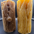 Two pillars of different colored beeswax candles on a dark surface