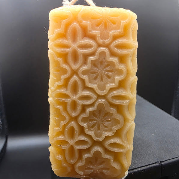 Rectangular beeswax candle with floral patterns on a dark background.