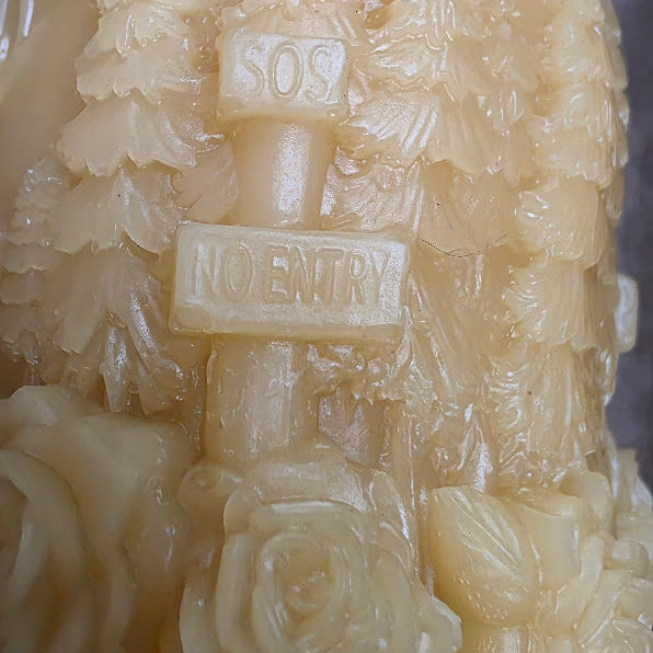 Close-up of a candle with 'SOS' and 'No Entry' signs, surrounded by floral patterns.