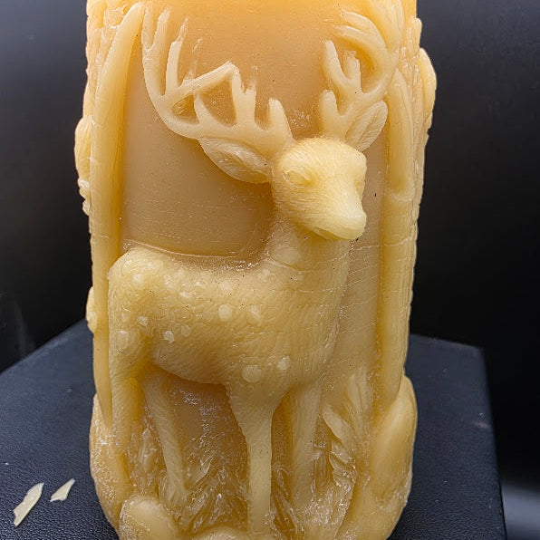 Beeswax candle with a deer design on a dark surface