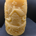 Beeswax candle with intricate carvings of a house and landscape on a black surface.