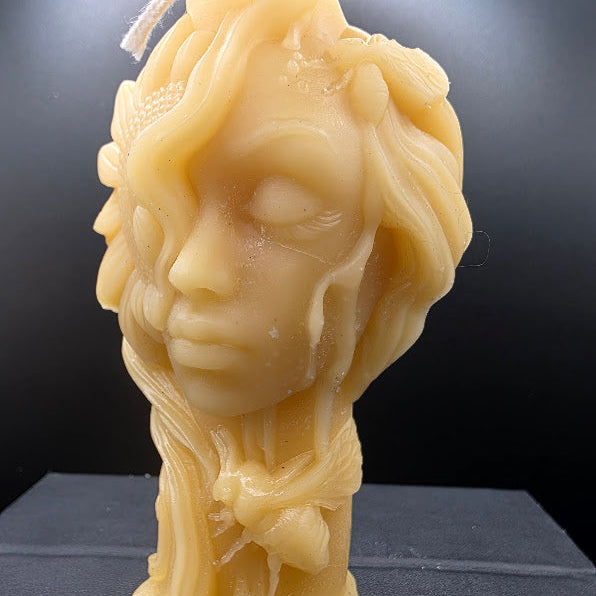Beige candle shaped like a stylized face with long hair on a dark background