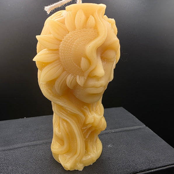 Beige candle with a stylized head and flower on a black surface with a dark background