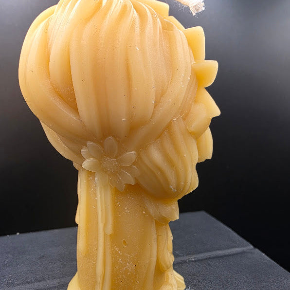Beige candle shaped like a girlwith braided hair on a dark surface