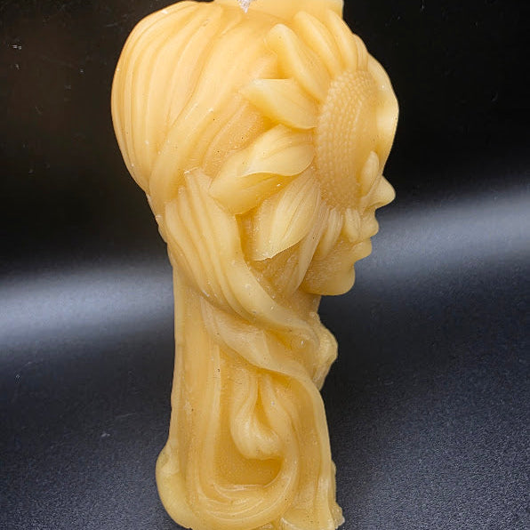 Beeswax candle shaped like a face with braided hair on a dark background