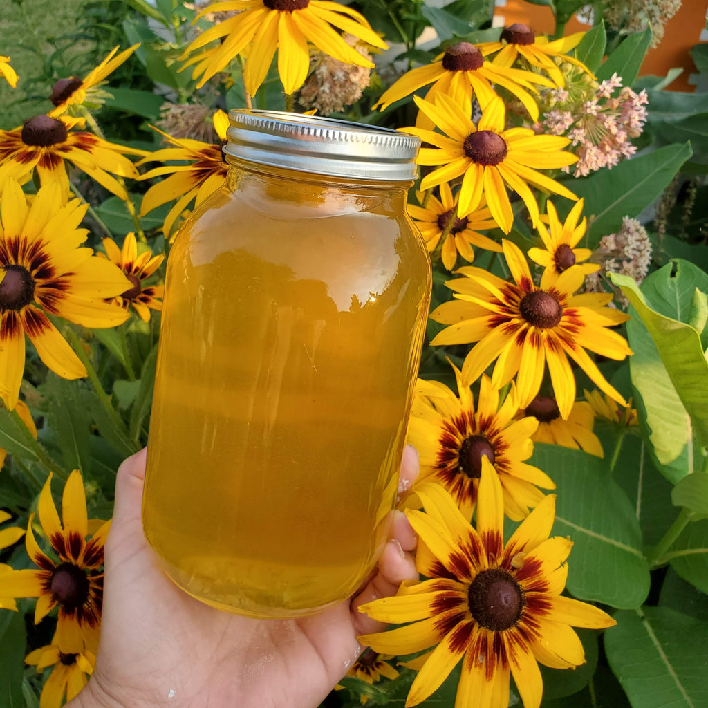 Hand holding a jar of honey with yellow flowers in the background