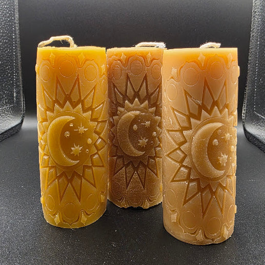 Three beeswax candles with moon design on a dark background.