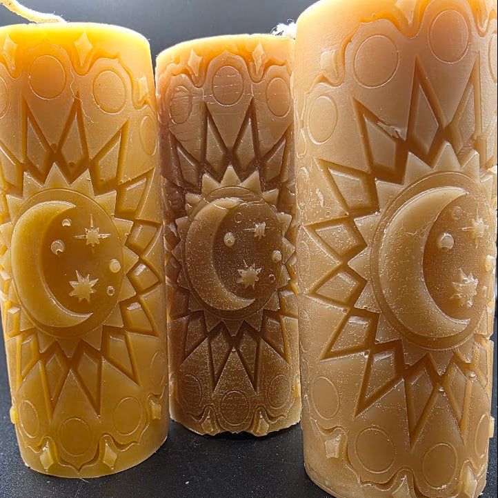 Three beeswax candles with celestial designs on a dark background.