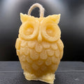 Beige owl-shaped candle on a dark textured surface with a blurred background