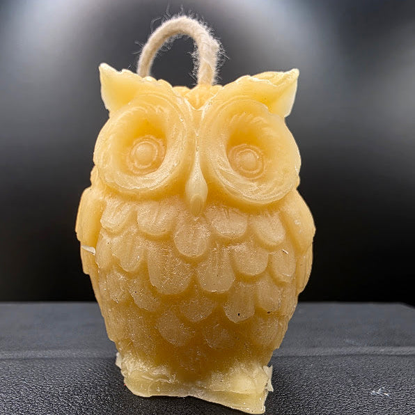 Beige owl-shaped candle on a dark textured surface with a blurred background